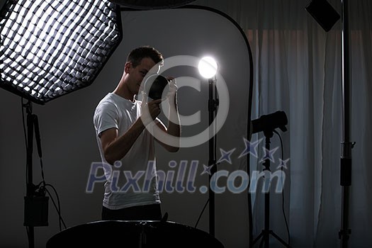 Young pro photographer with digital camera - DSLR and a huge telephoto lens in her well equiped studio, taking photos (color toned image; shallow DOF)