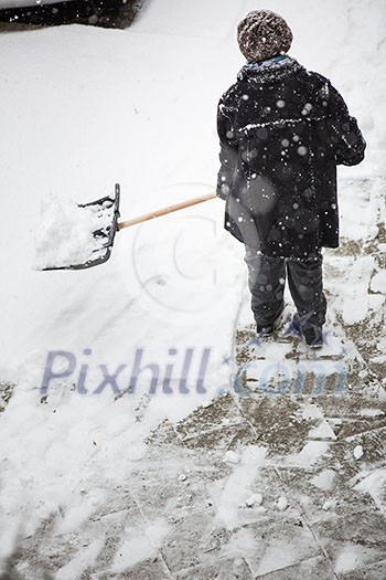 Man shoveling snow from the sidewalk in front of his house after a heavy snowfall in a city