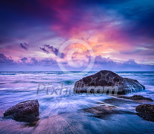 Tropical beach vacation background - waves and rocks on beach on sunset with beautiful cloudscape