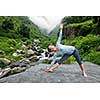 Woman doing Ashtanga Vinyasa yoga asana Utthita trikonasana - extended triangle pose outdoors at waterfall in Himalayas