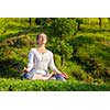 Young sporty fit woman doing yoga outdoors - meditating and relaxing in Padmasana Lotus Pose with chin mudra on green grass in forest