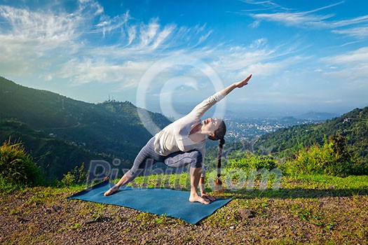Sporty fit woman practices yoga asana Utthita Parsvakonasana - extended side angle pose outdoors in mountains in the morning Sporty fit woman practices yoga asana Utthita Parsvakonasana - extended side angle pose outdoors in mountains in the morning