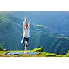 Woman practices balance yoga asana Vrikshasana tree pose in Himalayas mountains outdoors in the morning. Himachal Pradesh, India