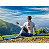 Sporty fit woman practices yoga asana Parivrtta Marichyasana -  seated spinal twist outdoors in mountains in the  morning