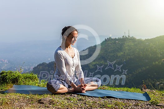 Sporty fit woman practices yoga asana Baddha Konasana - bound angle pose outdoors in Himalayas mountains in the morning. Himachal Pradesh, India Sporty fit woman practices yoga asana Baddha Konasana - bound angle pose outdoors in Himalayas mountains in the morning. Himachal Pradesh, India