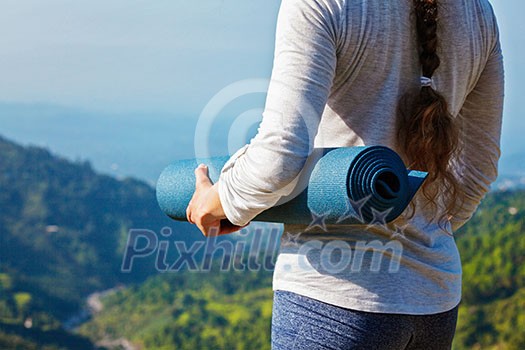 Woman standing with yoga mat outdoors in mountains close up with copyspace getting ready for yoga exercise Woman standing with yoga mat outdoors in mountains close up with copyspace getting ready for yoga exercise