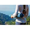 Woman standing with yoga mat outdoors in mountains close up with copyspace getting ready for yoga exercise