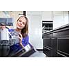 Pretty, young woman in her modern and well equiped kitchen putting cups into the dishwasher - an appliance that helps her keep the home tidy