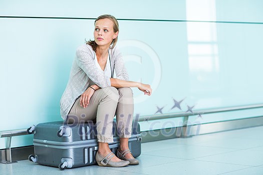 Young, female frustrated passenger at the airport, waiting desperately for her delayed flight (color toned image; shallow DOF)