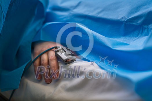 Detail of a hand of a patient being monitored dusing surgery - vital functions of the body are being closely watched by the anaesthesiologist (color toned image, shallow DOF)
