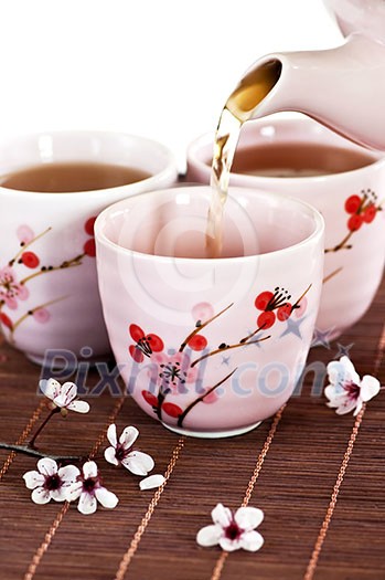 Pouring green tea into cups with cherry blossom design