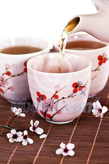 Pouring green tea into cups with cherry blossom design Pouring green tea into cups with cherry blossom design