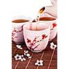 Pouring green tea into cups with cherry blossom design