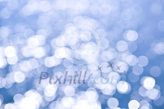 Out of focus bokeh background of blue water with sun reflections. Can be used as Christmas or winter backdrop.