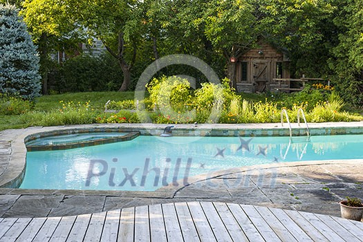 Backyard with outdoor inground residential swimming pool, garden, deck and stone patio Backyard with outdoor inground residential swimming pool, garden, deck and stone patio