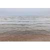 Waves coming to shore on foggy beach with fog over water.