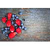Wild strawberries and blueberries on old blue wooden background with copy space