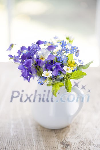 Bouquet of wild flowers in white vase on rustic wooden table near window, natural light