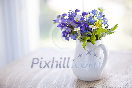 Bouquet of wild flowers in white vase on rustic wooden table near window with copy space, natural light
