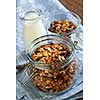 Homemade granola in open glass jar and milk or yogurt  on table with linens