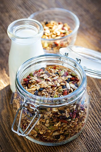 Homemade granola in open glass jar and milk or yogurt  on rustic wooden background