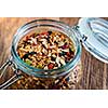 Homemade granola in open glass jar on rustic wooden background