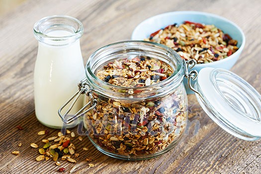 Homemade granola in open glass jar and milk or yogurt  on rustic wooden background