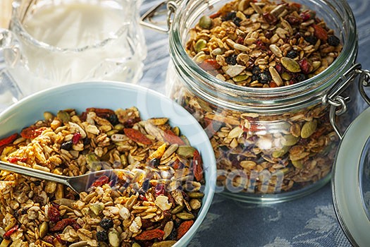 Serving of homemade granola in blue bowl and milk or yogurt on table with linens