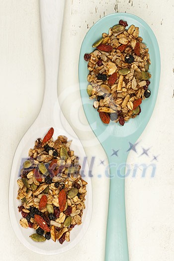 Homemade granola with various seeds and berries in two wooden spoons shot from above on wood background