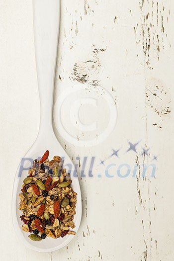 Homemade granola with various seeds and berries in white wooden spoon shot from above