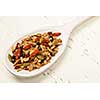 Toasted homemade granola with various seeds and berries in white wooden spoon on wood background