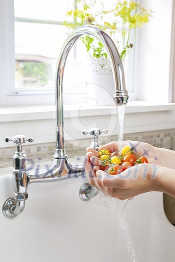 Hands washing fresh cherry tomatoes in running water of kitchen sink with curved faucet Hands washing fresh cherry tomatoes in running water of kitchen sink with curved faucet