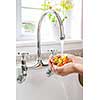 Hands washing fresh cherry tomatoes in running water of kitchen sink with curved faucet