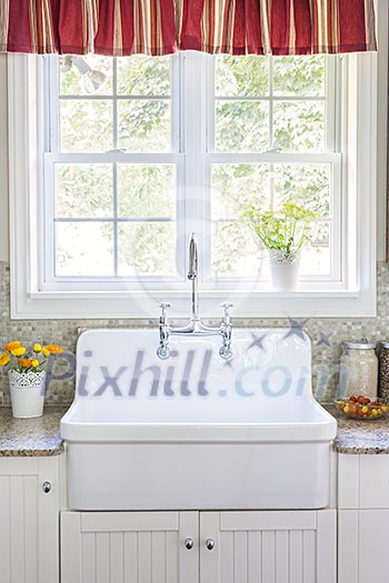 Kitchen interior with large rustic white porcelain sink and granite stone countertop under sunny window Kitchen interior with large rustic white porcelain sink and granite stone countertop under sunny window