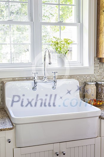 Kitchen interior with rustic white porcelain sink and granite stone countertop under large sunny window Kitchen interior with rustic white porcelain sink and granite stone countertop under large sunny window
