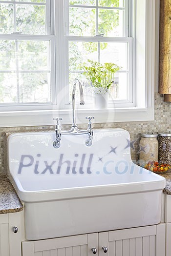 Kitchen interior with rustic white porcelain sink and granite stone countertop under large sunny window