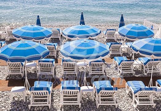 Blue umbrellas and chairs on pebble beach in Nice, France.