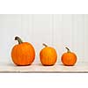 Three pumpkins of various sizes sitting in a row on white wooden background