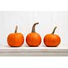 Three small pumpkins in a row against white background