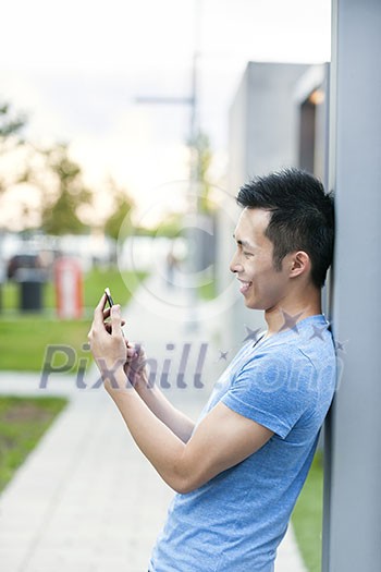 Young asian man smiling and looking at smart phone on city sidewalk