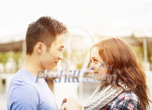 Romantic interracial young couple holding hands and looking at each other outside in sunset light Romantic interracial young couple holding hands and looking at each other outside in sunset light