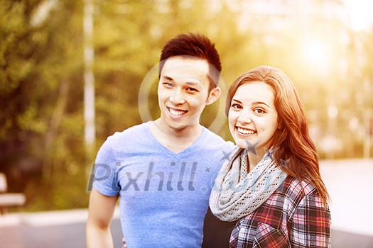 Romantic interracial young couple standing together and looking at camera outside in sunset light