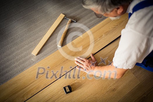DIY, repair, building and home concept - close up of male hands lying parquet floor board/laminate flooring (shallow DOF; color toned image)
