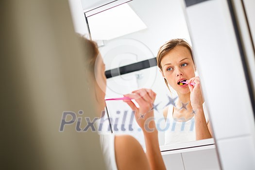 Pretty female brushing her teeth in front of mirror in the morning