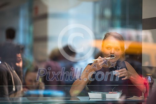 Pretty, young woman eating sushi in a restaurant, having her lunch break, enjoying the food, pausing for a while from her busy corporate/office life (color toned image) Pretty, young woman eating sushi in a restaurant, having her lunch break, enjoying the food, pausing for a while from her busy corporate/office life (color toned image)