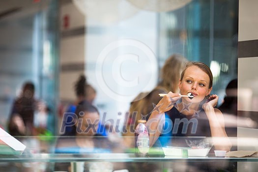 Pretty, young woman eating sushi in a restaurant, having her lunch break, enjoying the food, pausing for a while from her busy corporate/office life (color toned image)