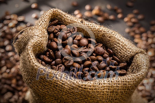 spilled coffee beans in bag on wooden table. Morning light spilled coffee beans in bag on wooden table. Morning light