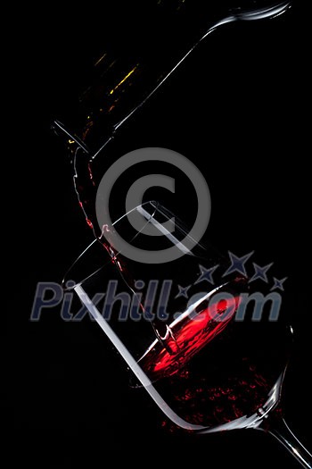 red wine pouring into wine glass isolated on black
