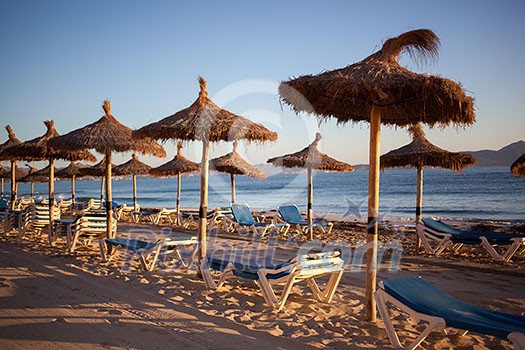 Empty beach with straw umbrellas on sunrise in Spain, Mallorca