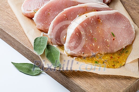 Raw meat. Pork escalope with sause made of honey and herbs with green sage leaves on wooden board against white background. Top view Raw meat. Pork escalope with sause made of honey and herbs with green sage leaves on wooden board against white background. Top view